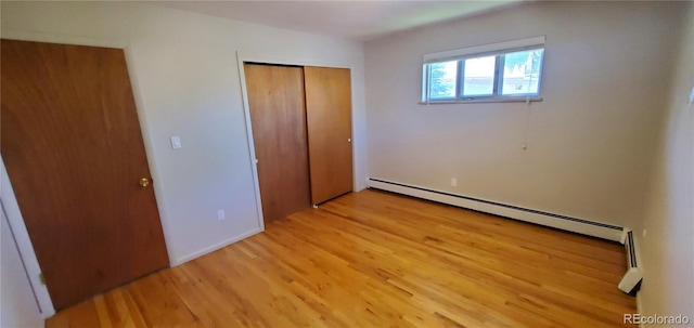 unfurnished bedroom with light wood finished floors, a closet, and baseboard heating