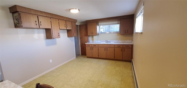 kitchen featuring brown cabinetry, light floors, baseboards, a baseboard radiator, and light countertops