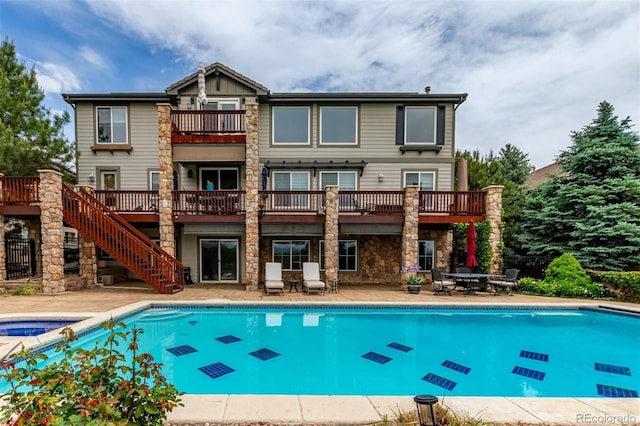 8993 Stonecrest Way, Highlands Ranch, CO 80129 - back of house featuring a balcony, stone siding, a patio, a pool with connected hot tub, and stairway