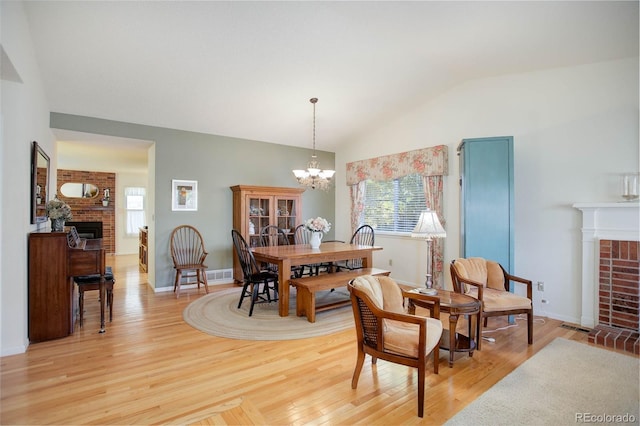 dining room with a chandelier, lofted ceiling, light wood-type flooring, and a brick fireplace