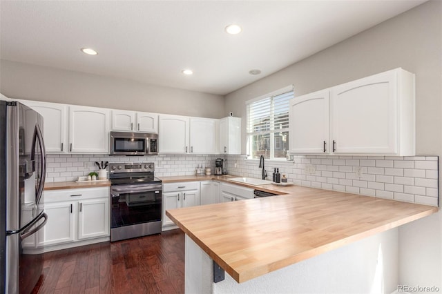 kitchen with a sink, wood counters, white cabinetry, appliances with stainless steel finishes, and a peninsula