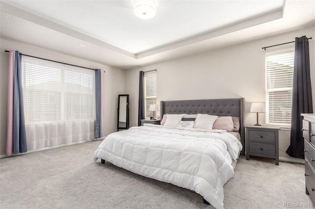 bedroom with a tray ceiling, multiple windows, and light colored carpet