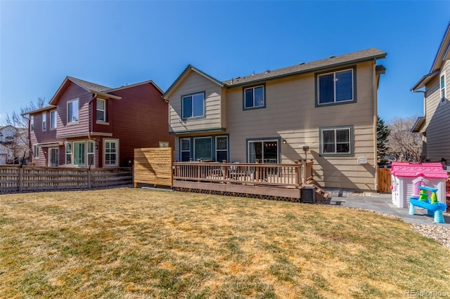 back of property with a wooden deck, a yard, and fence