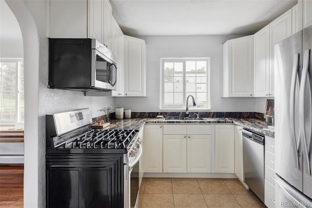 2895 S Sherman St, Englewood, CO 80113 - kitchen with appliances with stainless steel finishes, white cabinets, arched walkways, a baseboard radiator, and light tile patterned floors
