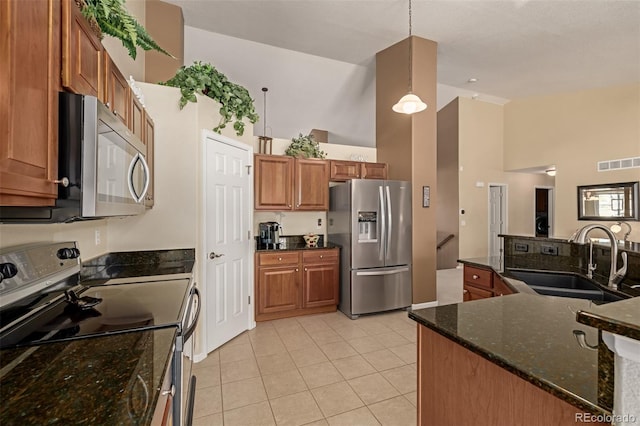 kitchen with stainless steel appliances, dark stone counters, sink, hanging light fixtures, and light tile patterned floors