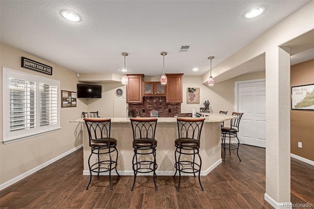 kitchen with a breakfast bar area, backsplash, decorative light fixtures, dark wood-type flooring, and light stone counters