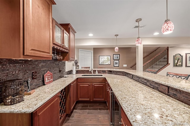 bar with decorative backsplash, beverage cooler, light stone countertops, pendant lighting, and sink