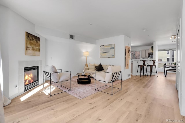 living room featuring a glass covered fireplace, visible vents, and light wood-type flooring
