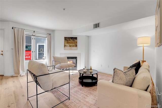 living area with a tiled fireplace, visible vents, light wood-style flooring, and baseboards