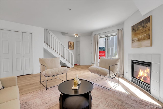 living room featuring a tiled fireplace, stairway, light wood-style floors, and baseboards