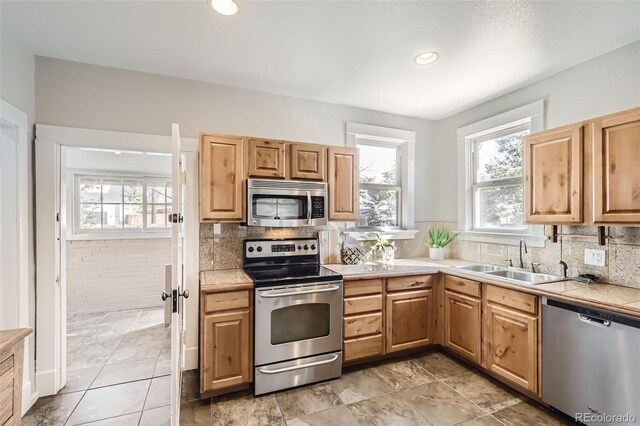 kitchen with appliances with stainless steel finishes, light tile patterned flooring, decorative backsplash, and sink