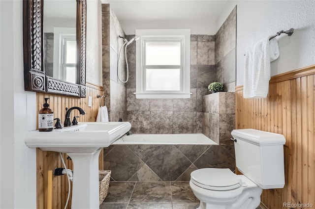 bathroom featuring tiled shower / bath combo, toilet, and wood walls