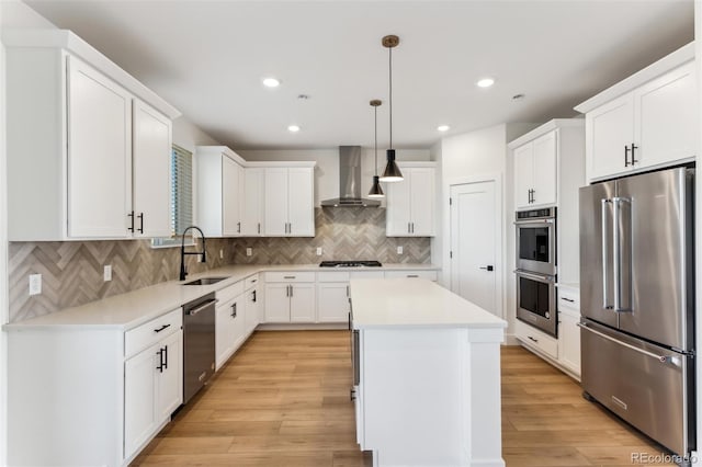 kitchen with stainless steel appliances, light wood-style floors, a sink, wall chimney range hood, and a kitchen island