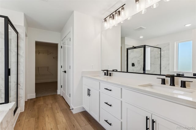 bathroom with a walk in closet, a sink, a shower stall, and wood finished floors