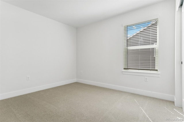 spare room featuring light carpet and baseboards