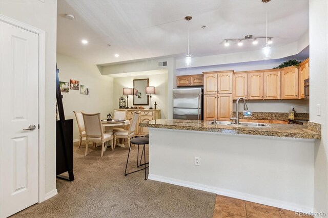 kitchen with stainless steel fridge, a sink, light brown cabinets, a peninsula, and baseboards