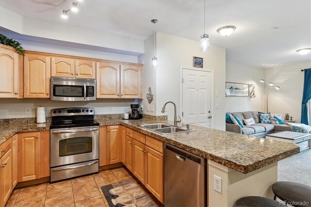 kitchen with a peninsula, light brown cabinets, open floor plan, a sink, and appliances with stainless steel finishes
