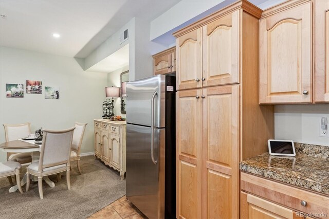 kitchen featuring light colored carpet, visible vents, freestanding refrigerator, dark stone counters, and light brown cabinets