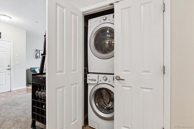 washroom featuring laundry area, stacked washer / dryer, baseboards, tile patterned floors, and carpet