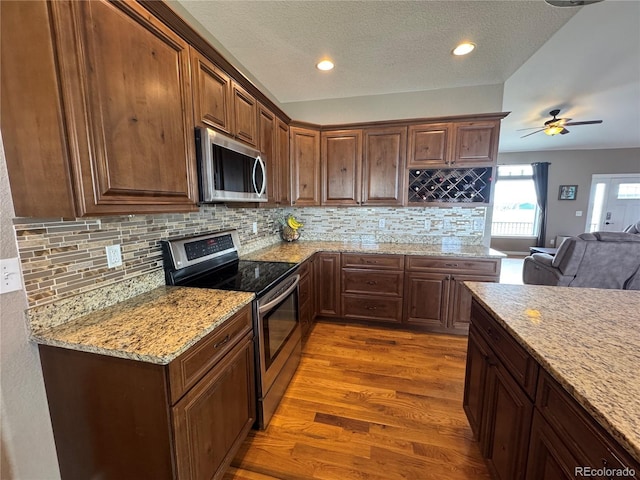 kitchen with light stone countertops, open floor plan, decorative backsplash, light wood-style floors, and stainless steel appliances