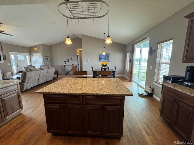 kitchen with lofted ceiling, wood finished floors, a center island, hanging light fixtures, and dark brown cabinets