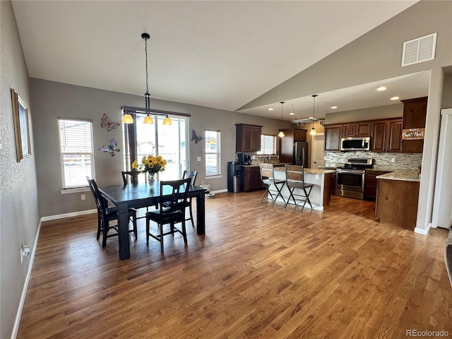 dining room featuring plenty of natural light, baseboards, visible vents, vaulted ceiling, and wood finished floors