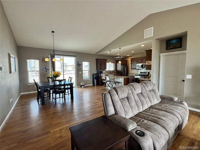 living area featuring baseboards, dark wood-type flooring, visible vents, vaulted ceiling, and a notable chandelier