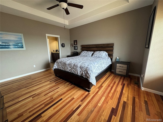 bedroom with a raised ceiling, baseboards, light wood-type flooring, and a ceiling fan