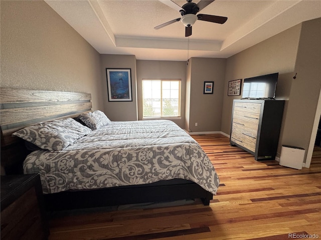 bedroom featuring baseboards, a raised ceiling, light wood-type flooring, and a ceiling fan