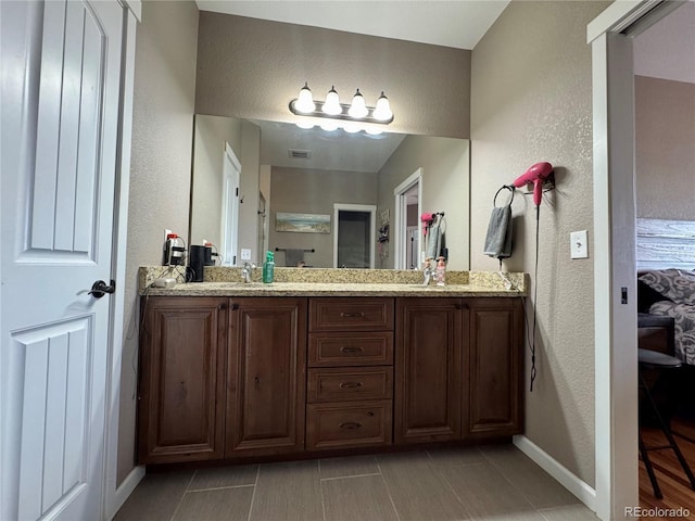 ensuite bathroom with visible vents, a textured wall, a shower stall, double vanity, and baseboards