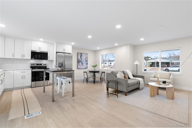 kitchen with white cabinetry, a breakfast bar area, backsplash, light hardwood / wood-style floors, and stainless steel appliances