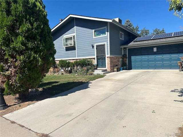 view of front of home with solar panels, stone siding, a garage, and driveway