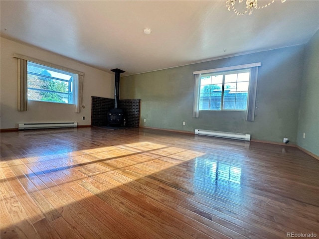 unfurnished living room with wood-type flooring, a baseboard radiator, a wealth of natural light, and a wood stove