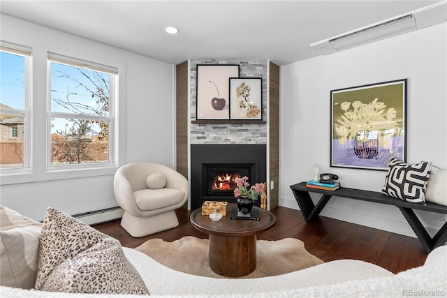 living room featuring a large fireplace, dark hardwood / wood-style floors, and a baseboard heating unit