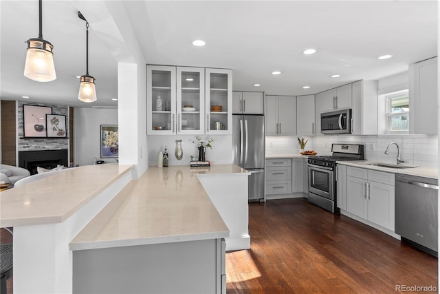 kitchen featuring kitchen peninsula, appliances with stainless steel finishes, dark hardwood / wood-style flooring, a fireplace, and hanging light fixtures