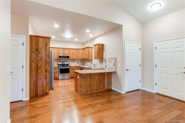 107 Carina Cir, Loveland, CO 80537 - kitchen with appliances with stainless steel finishes, a peninsula, vaulted ceiling, tasteful backsplash, and light wood-style floors
