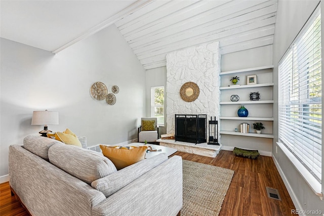living area with wood finished floors, a stone fireplace, lofted ceiling, and baseboards