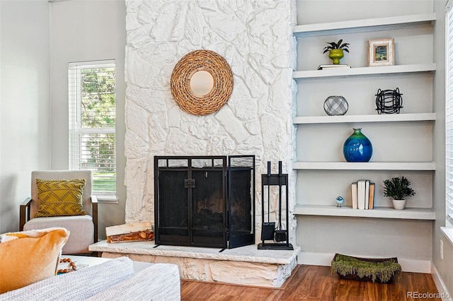 living room featuring wood finished floors, a stone fireplace, built in features, and baseboards