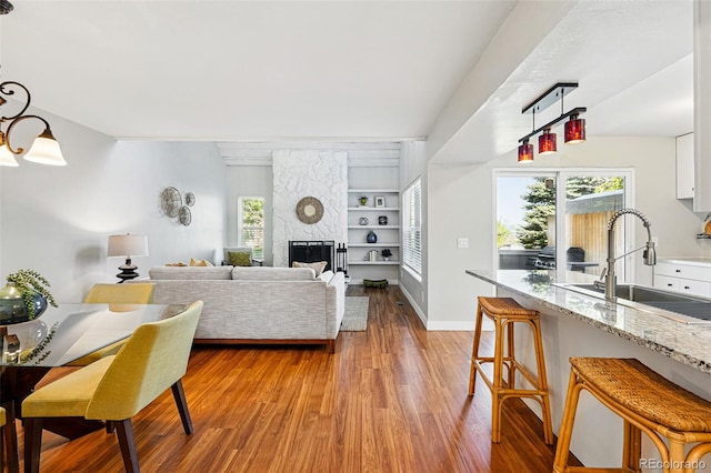 living room featuring wood finished floors, built in shelves, a stone fireplace, and baseboards