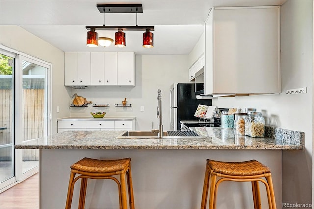 kitchen featuring a sink, a peninsula, white cabinets, light stone countertops, and a breakfast bar