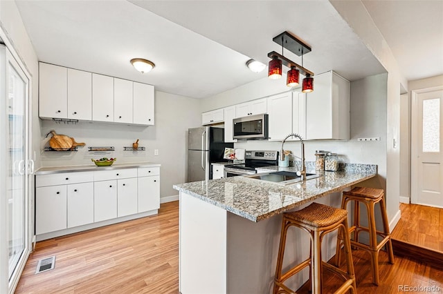 kitchen with appliances with stainless steel finishes, a sink, light wood-style floors, a kitchen bar, and a peninsula
