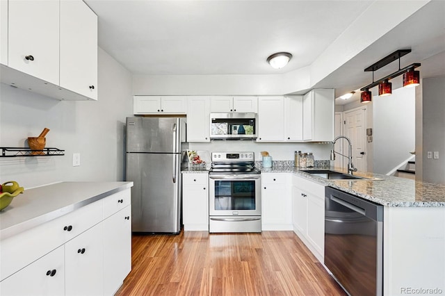 kitchen featuring appliances with stainless steel finishes, a sink, a peninsula, light wood finished floors, and white cabinetry