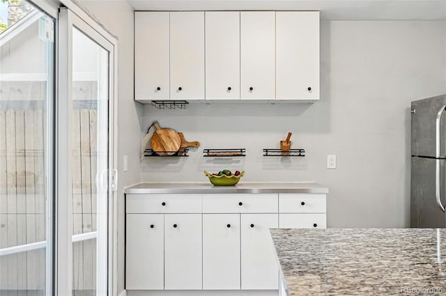 kitchen with freestanding refrigerator, white cabinetry, and stainless steel countertops