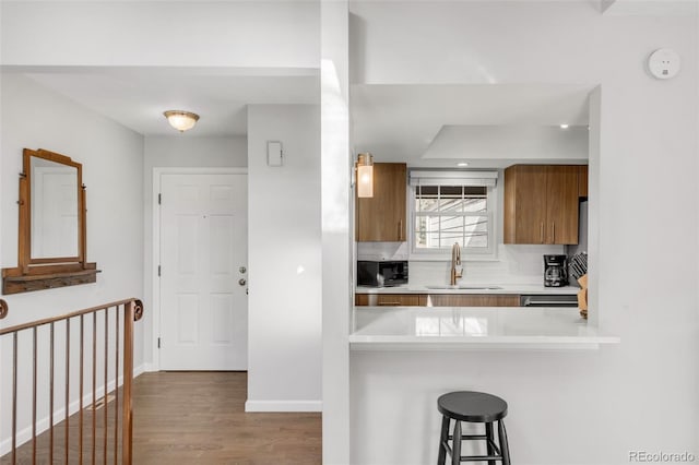 kitchen with brown cabinetry, a breakfast bar area, light countertops, black microwave, and a sink