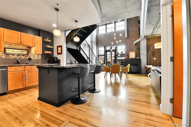 kitchen featuring light wood-style flooring, decorative backsplash, brick wall, dishwasher, and a kitchen breakfast bar