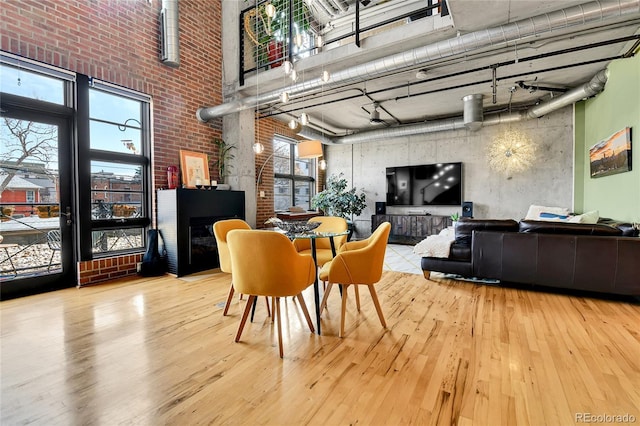 dining area with a glass covered fireplace, a towering ceiling, brick wall, and wood finished floors