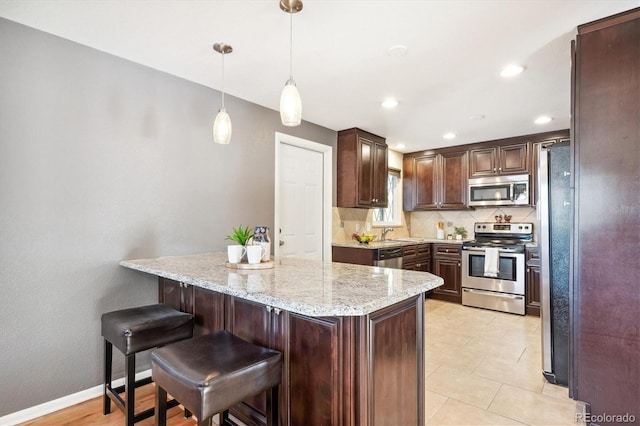 kitchen featuring stainless steel appliances, pendant lighting, light stone countertops, decorative backsplash, and sink