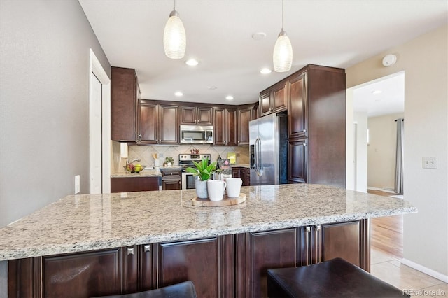 kitchen featuring decorative backsplash, stainless steel appliances, decorative light fixtures, and light stone countertops