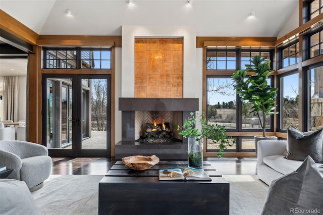 living area with high vaulted ceiling, a warm lit fireplace, french doors, and wood finished floors