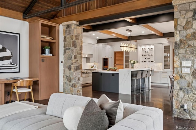 living area with beamed ceiling, dark wood-style flooring, an inviting chandelier, and ornate columns